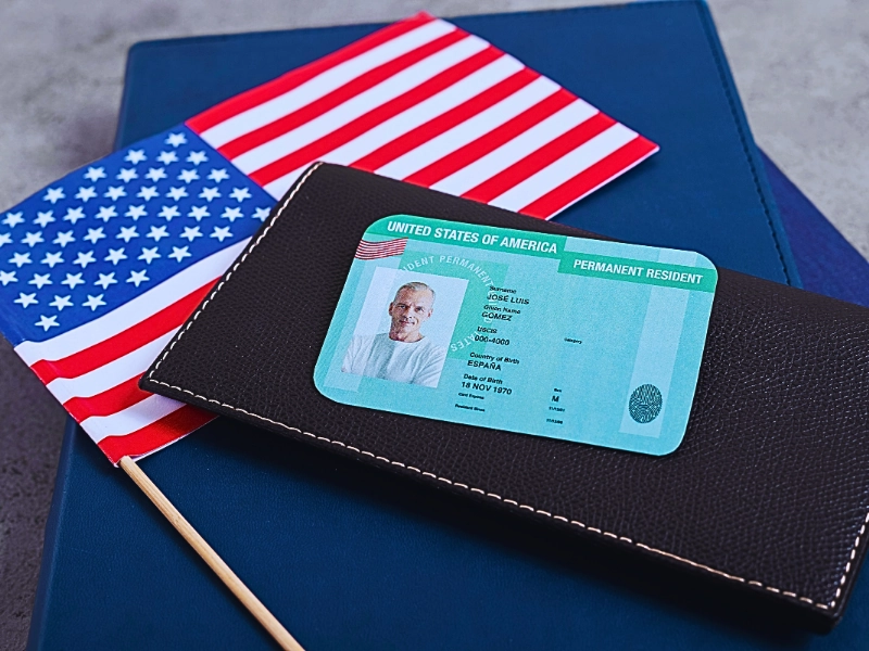 Top view of green card on a black wallet and American flag. Get a Green Card Through Marriage If You Overstayed a Visa