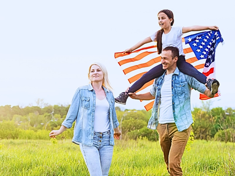 How USCIS Decides Whether a Marriage Is “Bona Fide” for a Green Card 1 Family walking in field with American flag.